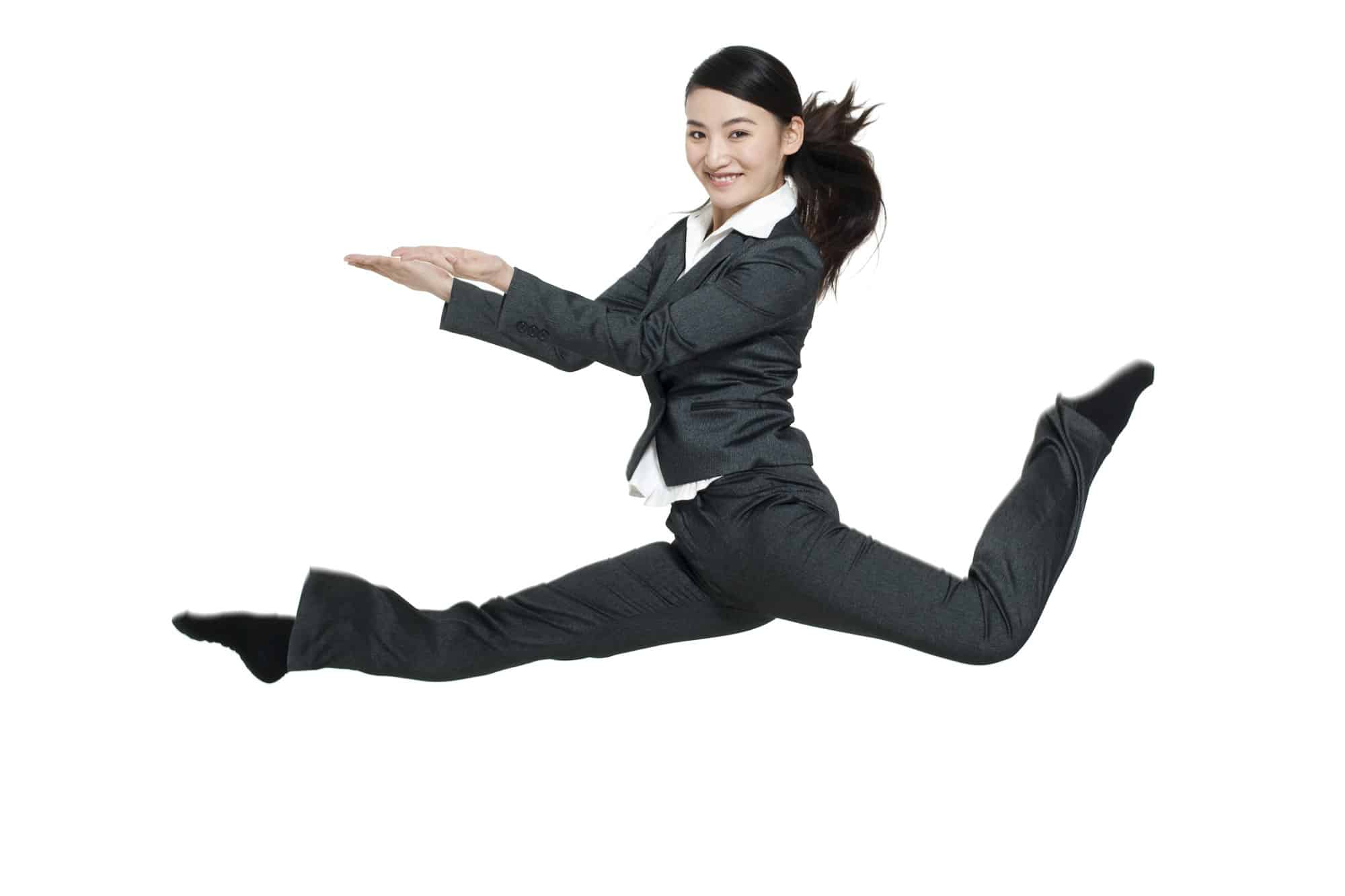 Flex CMO Une femme en costume d'affaires, incarnant l'énergie dynamique d'un CMO Flex, effectue un saut en l'air sur un fond blanc, étendant ses bras et ses jambes.